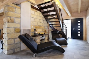 Ein Zimmer mit einer Steinwand, einem schwarzen Massagesessel, einer Holztreppe und einer schwarzen Tür.