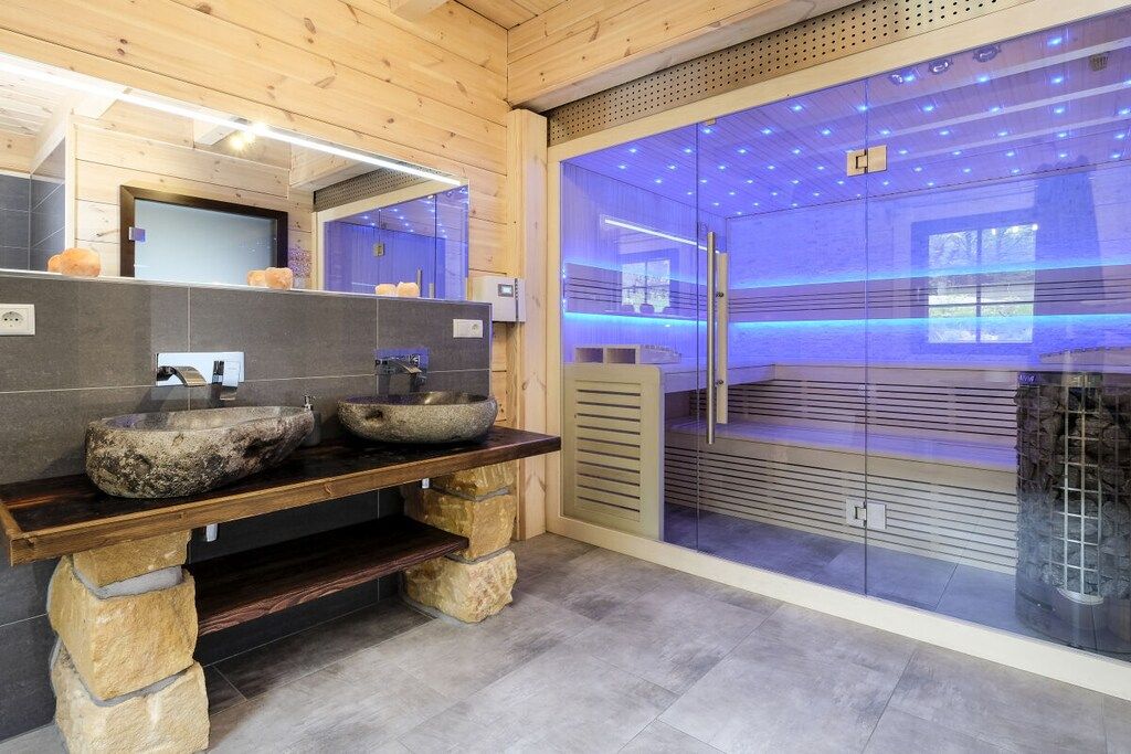 A modern bathroom with stone sinks, a wooden vanity, and a glass shower enclosure with blue lighting.