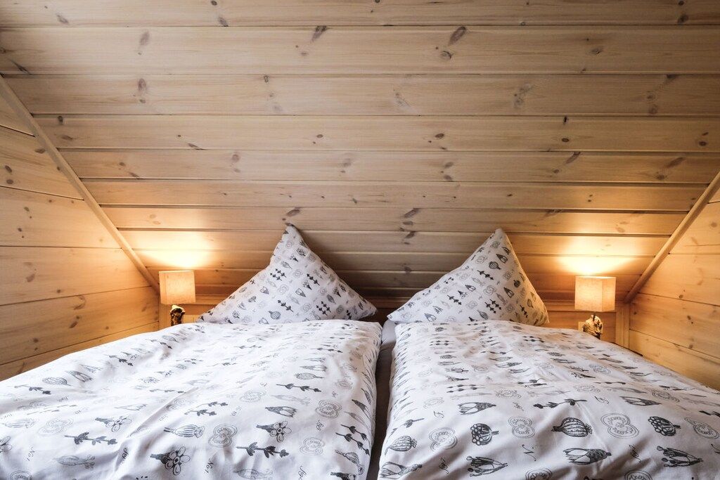 Une pièce avec un plafond en pente, deux lits avec une literie à motifs et des lampes fixées au mur.