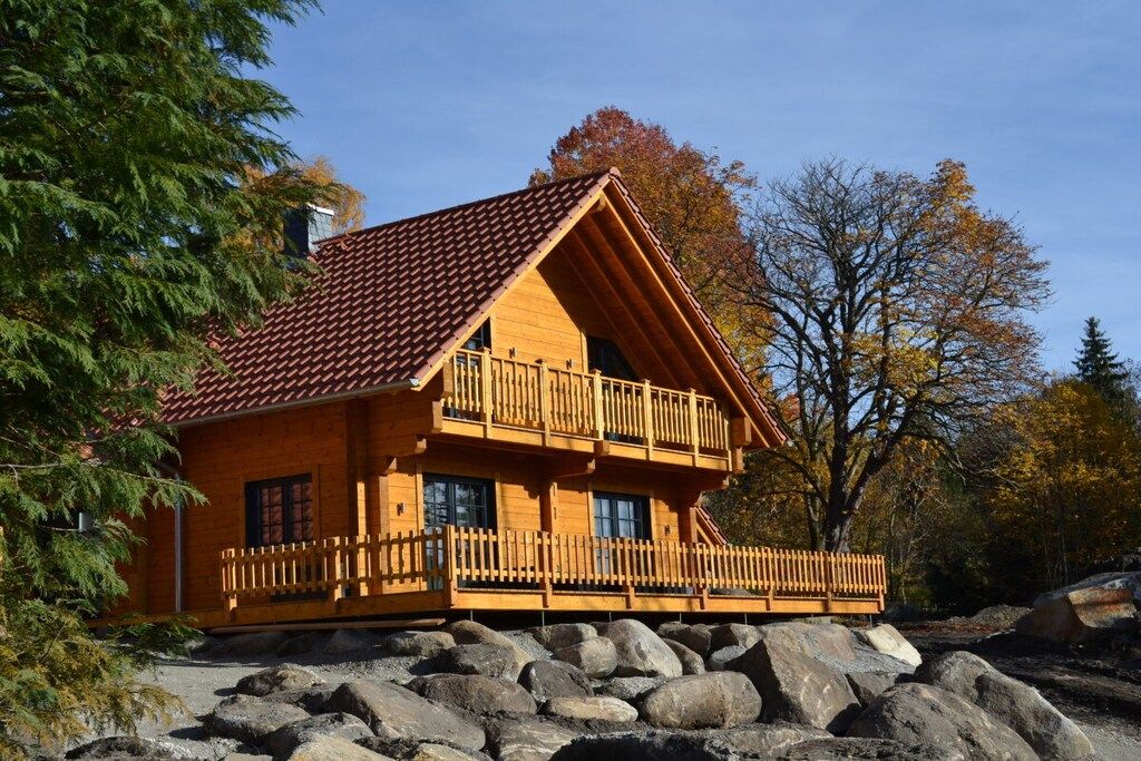 A wooden cabin with a balcony, situated on a rocky terrain with trees in the background.