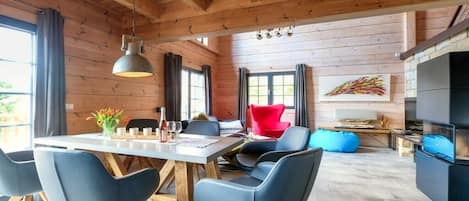 Ein modernes Interieur mit Holzboden, einem Essbereich mit Tisch und Stühlen, einem roten Sessel und einem Kamin.