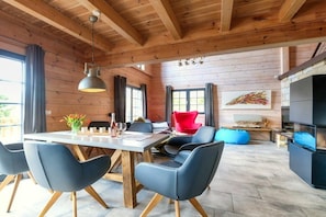 Ein modernes Interieur mit Holzboden, einem Essbereich mit Tisch und Stühlen, einem roten Sessel und einem Kamin.