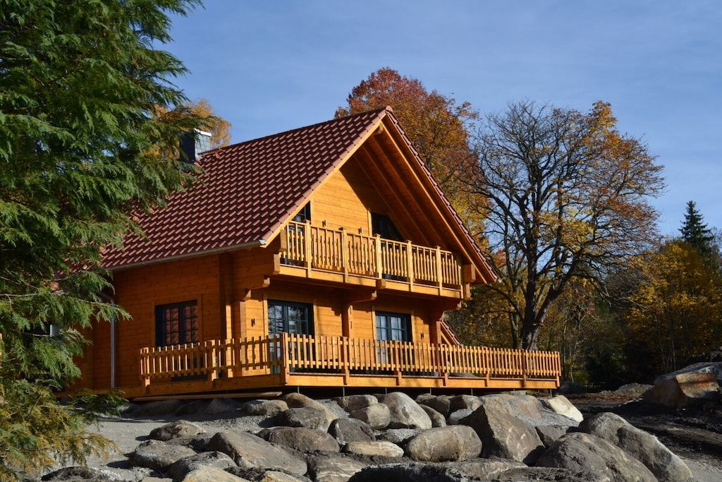 Une cabane en bois dotée d’un balcon, située sur un terrain rocheux, avec des arbres en arrière-plan.