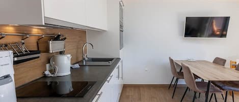 A modern kitchen with white cabinets, a coffee maker, and a dining area with a wooden table and chairs.