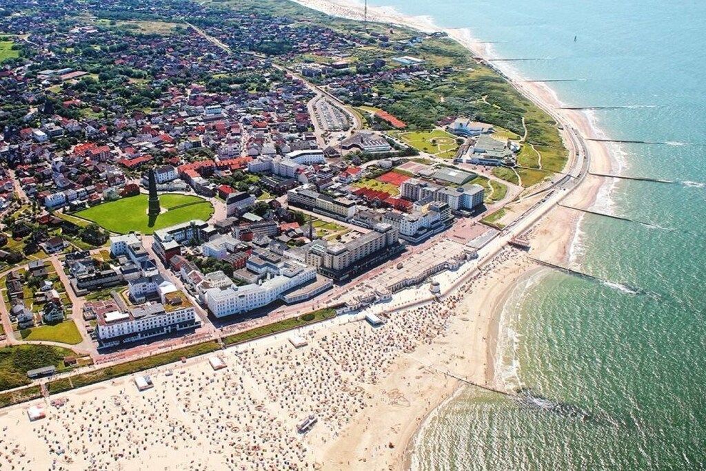 Vue aérienne d’une ville côtière avec une plage, des zones résidentielles et un grand ensemble immobilier.
