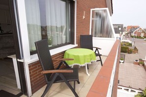 A balcony with a table and two chairs, a brick wall, and a window with curtains. - Apartment -Starfish- (Borkum)