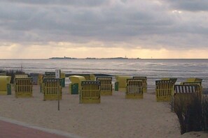 A beach with yellow beach chairs lined up on the sand, a clear view of the ocean, and a distant shoreline with structures. - Residence Albatros 28 (Cuxhaven)