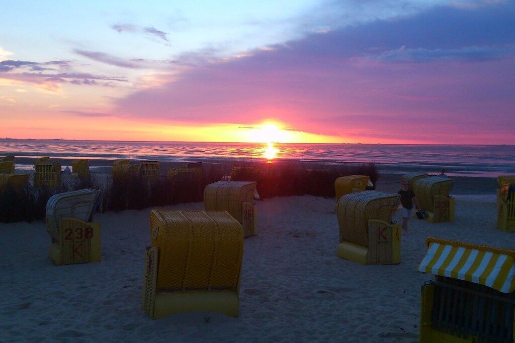 Ein Strand mit Korbstühlen und einem Sonnenuntergang im Hintergrund.