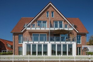 A two-story brick house with a white picket fence, large windows, and a balcony with an umbrella. - Holiday apartment in Juist with swimming pool (Juist)