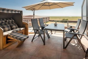 An outdoor patio with a checkered sofa, a table, and chairs, an umbrella, and a view of the landscape. - Holiday apartment in Juist with swimming pool (Juist)