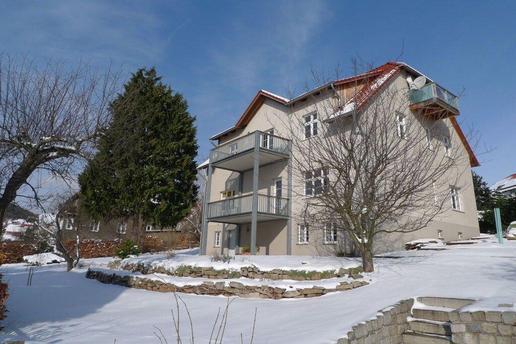 A two-story building with a balcony, surrounded by snow-covered ground and trees.