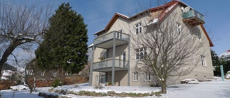 Un bâtiment à deux étages doté d’un balcon, entouré d’un paysage enneigé et d’arbres.