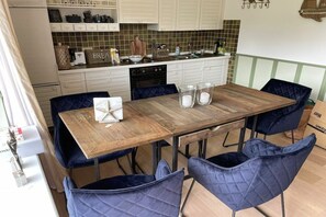 A dining area with a wooden table, four blue chairs, and a kitchen in the background. - Skellinghörn 24 Ground Floor (Morsum)