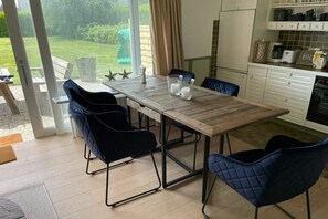 A modern kitchen with a wooden table, blue chairs, and a view of the garden through the glass door. - Skellinghörn 24 Ground Floor (Morsum)