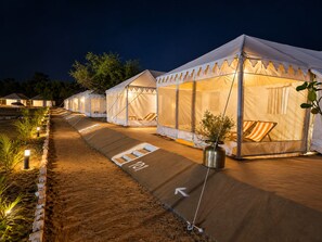 A row of tents with a paved walkway between them, each with a small table and chair. - Spirit Desert Camp Pushkar (Ajmer)