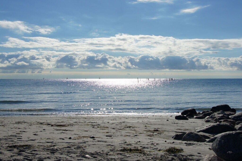 Ein Strand mit klarem Himmel, ruhiger See und felsiger Küste.