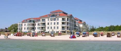 A multi-story hotel with balconies, located near a beach with beach chairs and a tent.