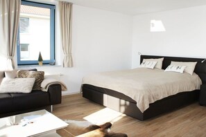 A bedroom with a bed, a sofa, a coffee table, and a window with curtains. - Holiday apartment with 1 bedroom (Fehmarn OT Burgtiefe)