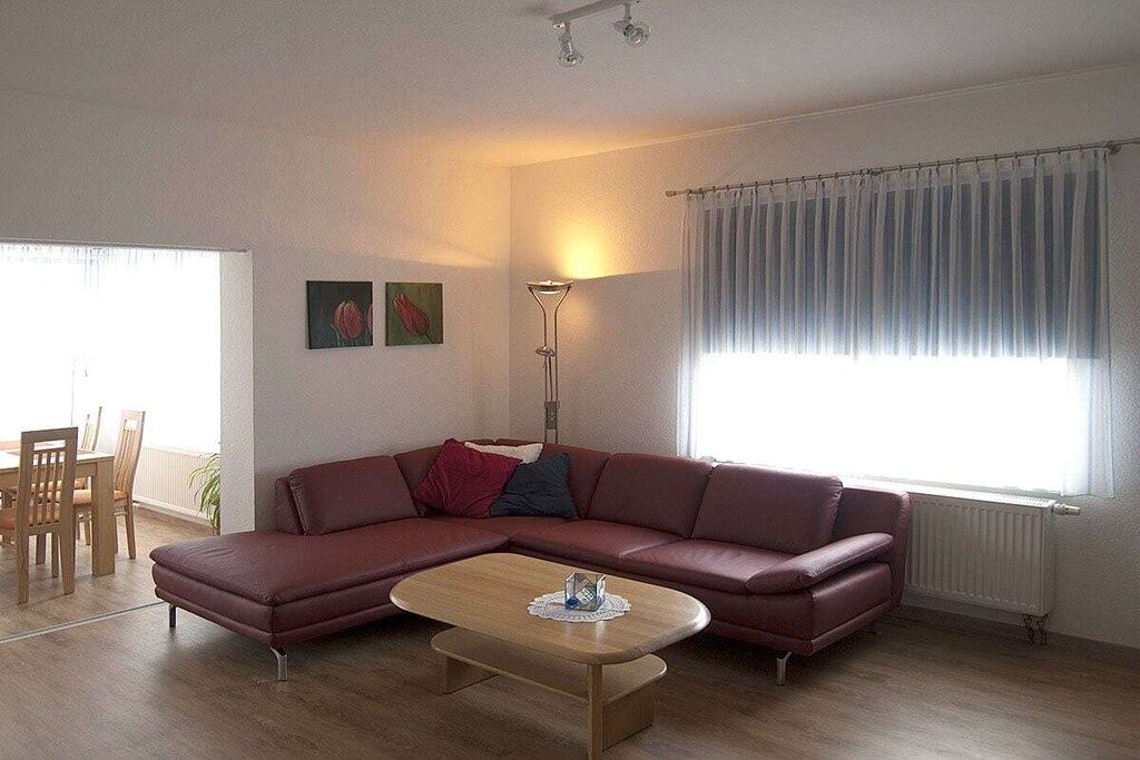 A living room with a sectional sofa, a coffee table, a dining area with chairs, and a window with curtains.