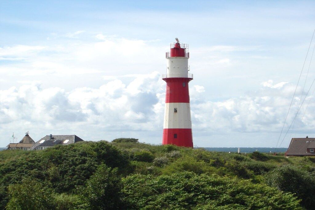 A lighthouse with a red and white color scheme, surrounded by greenery and a clear sky.