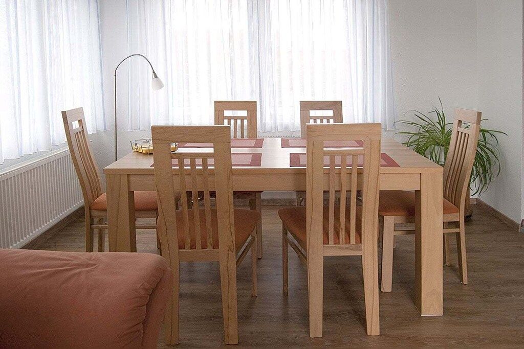 A dining area with a wooden table and chairs, a floor lamp, and a potted plant.