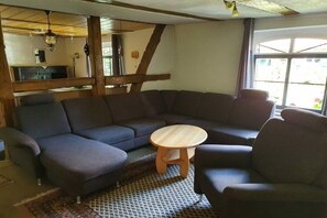 Un salon comprenant un canapé d’angle, une table basse ronde en bois et une fenêtre laissant entrer la lumière naturelle.