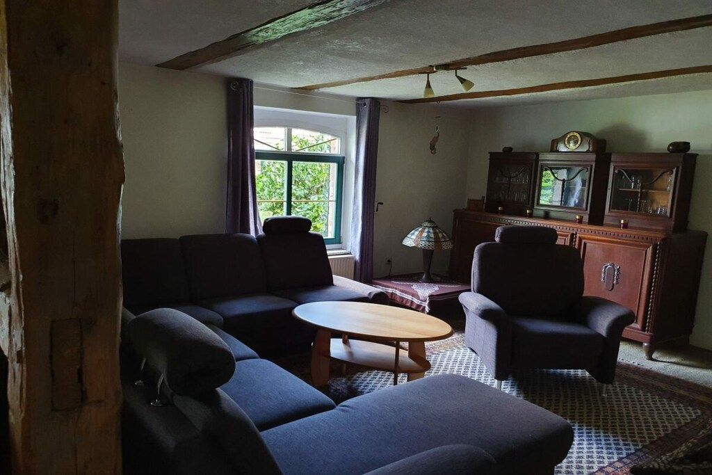 A room with a sofa, two armchairs, a small table, and a cabinet with a clock.