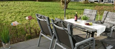 Un patio al aire libre con una mesa preparada para dos personas, rodeada de sillas, una botella de vino y una pequeña planta.