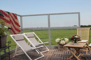 A deck with two lounge chairs, a small table with a vase of flowers, and a flag. - Holiday home with 3 bedrooms (Warnsdorf)