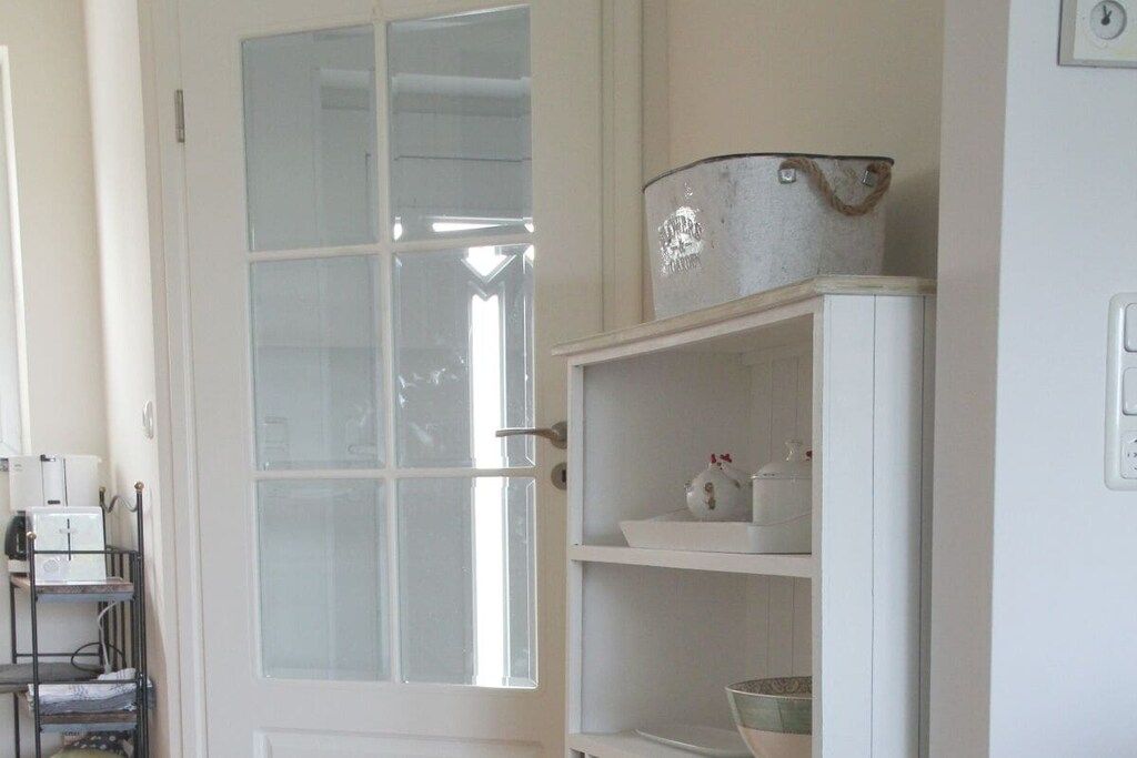 A room with a white door, a white shelf with kitchenware, and a white cabinet.