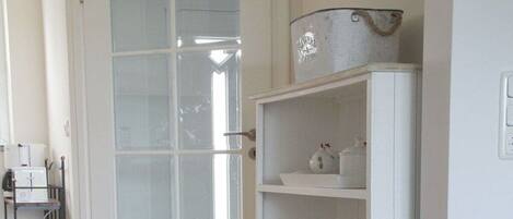 A room with a white door, a white shelf with kitchenware, and a white cabinet.