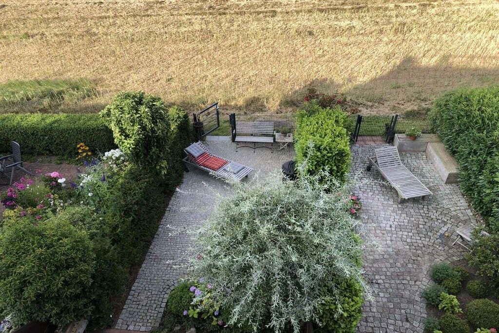 Een terras met een bank, een tafel en een kleine tuin vol planten en bloemen.