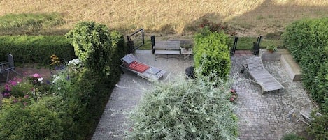 Een terras met een bank, een tafel en een kleine tuin vol planten en bloemen.