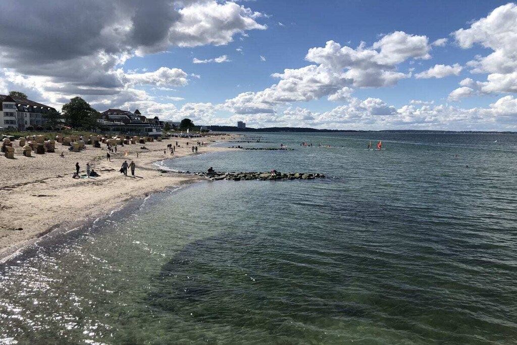 Een strand met helder water, een zandstrand en gebouwen op de achtergrond.