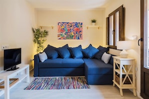 A living room with a dark blue sofa, a television, a colorful abstract painting, a potted plant, and a lamp on a side table.
