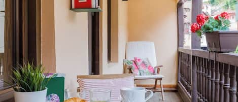 A balcony with a table set for breakfast, a chair, a small house model, and a potted plant.