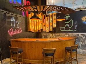 A bar area with a wooden counter, neon signs for cocktails and hookah, and three bar stools.