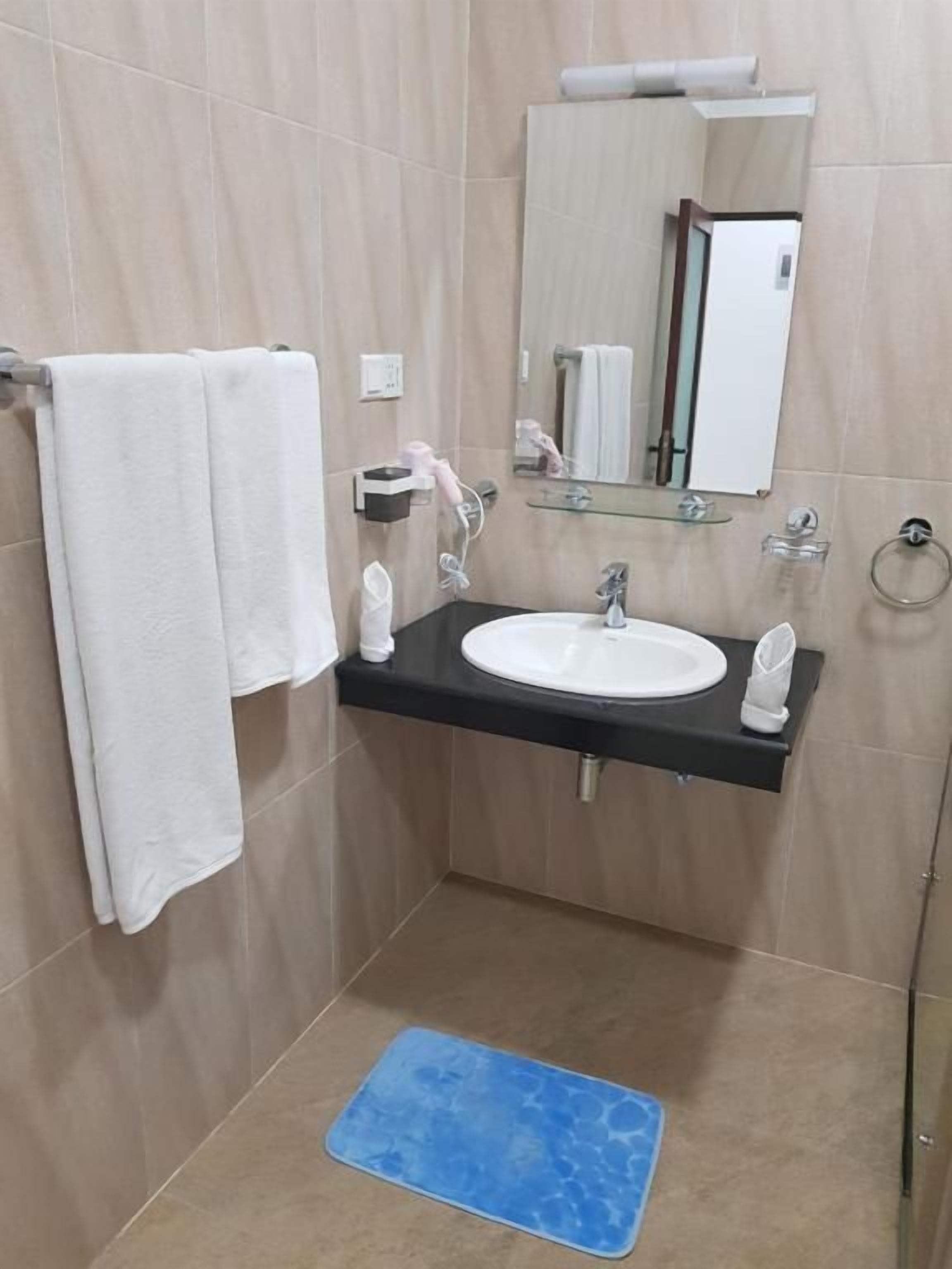 Un baño con lavamanos blanco, espejo y felpudo azul.