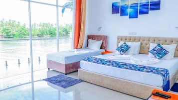 Habitación de hotel con un ventanal grande, cama con cubrecama de estampado azul y vista a una masa de agua.