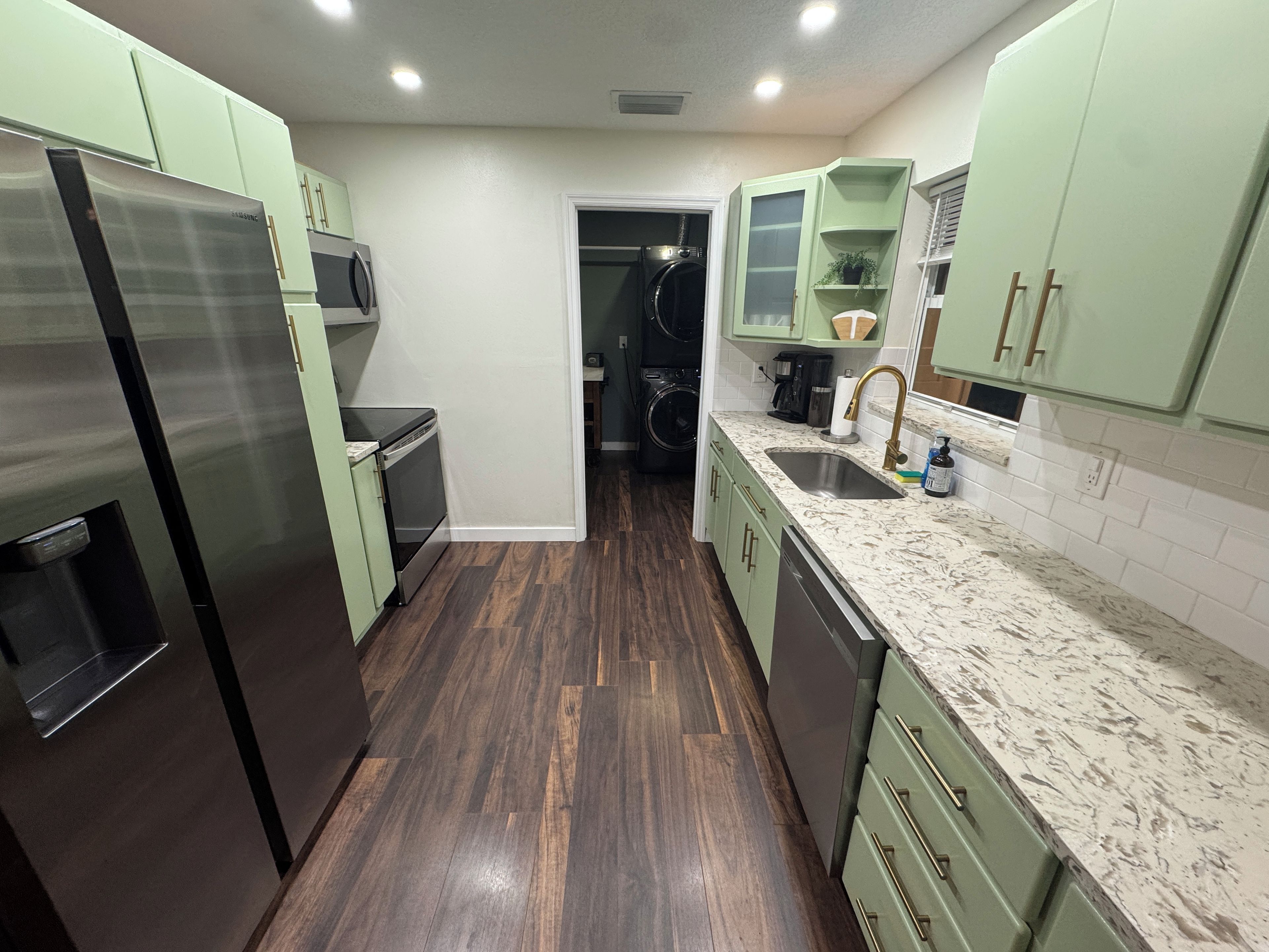 A kitchen with stainless steel appliances, green cabinets, a marble countertop, and a washing machine in the background.