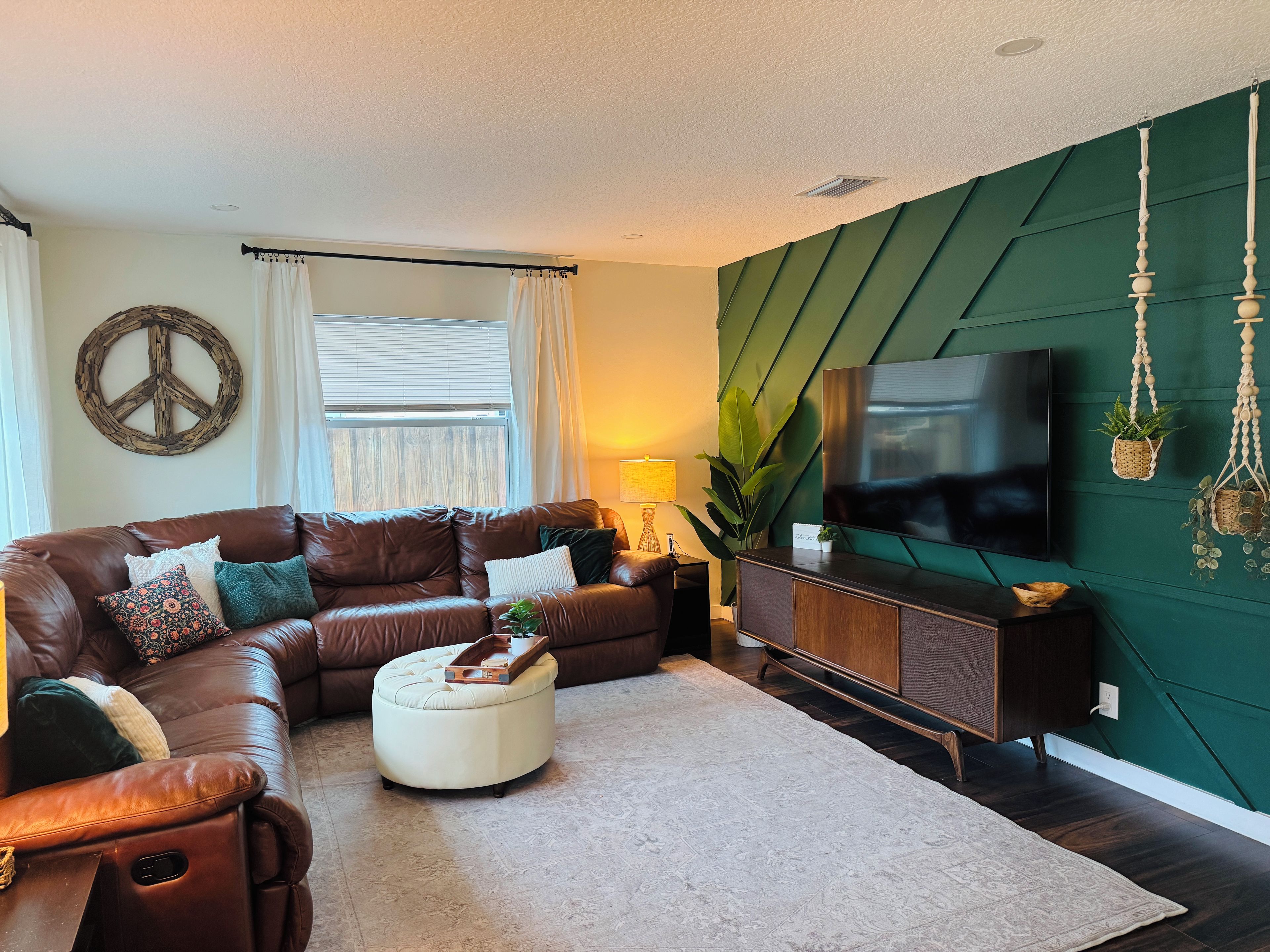 A living room with a brown leather sofa, a white ottoman, a flat-screen TV, and a green accent wall.