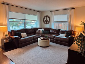 A living room with a brown leather sectional sofa, a white ottoman, and a patterned rug. - Spacious 4-bedroom house in peaceful Delray Beach minutes from Atlantic Ave! (Delray Beach)