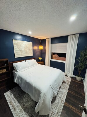 A bedroom with a bed, a nightstand, a map on the wall, a window with curtains, and a potted plant. - Spacious 4-bedroom house in peaceful Delray Beach minutes from Atlantic Ave! (Delray Beach)