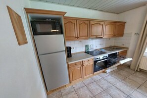 A kitchen with wooden cabinets, a refrigerator, a microwave, an oven, and a sink. - Holiday apartment with 1 bedroom (Butjadingen)