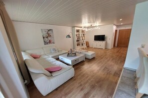 Ein Wohnzimmer mit Sofa, Couchtisch, Fernseher, Bücherregal und einer Treppe.