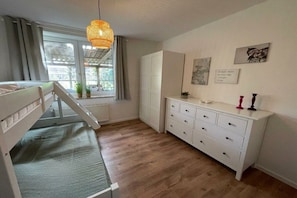 A bedroom with a bunk bed, a dresser, a window with curtains, and a hanging light fixture. - Holiday apartment with 1 bedroom (Butjadingen)