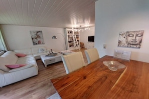 A modern living room with a wooden dining table, white sofa, and a bookshelf. - Holiday apartment with 1 bedroom (Butjadingen)