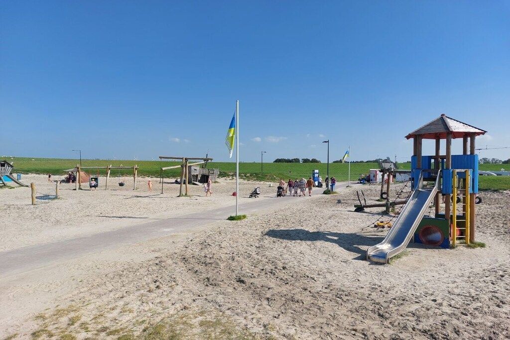 A sandy beach with a playground, including a slide and a small pavilion.