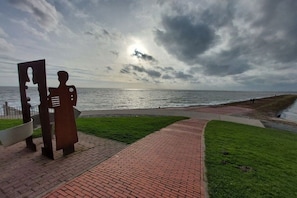 A paved walkway leading to a grassy area with a sculpture of a human figure. - Holiday apartment with 1 bedroom (Butjadingen)