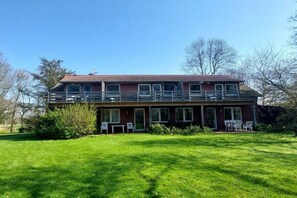 A two-story house with a balcony on the upper floor, a front lawn, and a satellite dish on the roof. - Holiday apartment with 1 bedroom (Butjadingen)